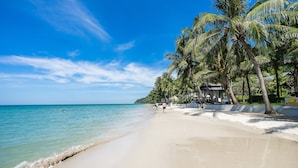 A beach with palm trees, a clear sky, and a few people walking. - KC Grande Resort Koh Chang (Ko Chang)
