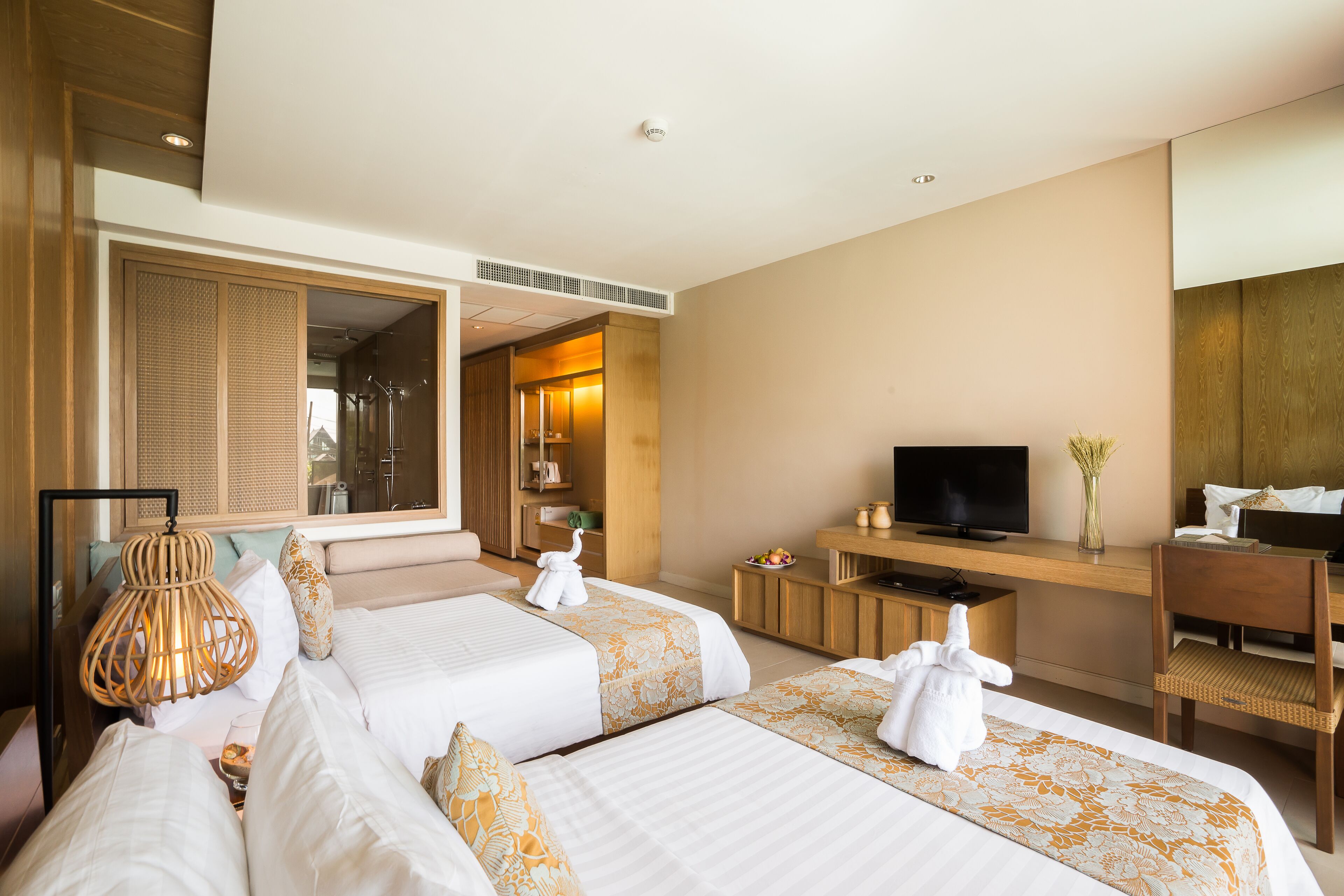 A hotel room with two beds, a TV, a desk, and a bathroom visible through an open door.