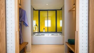 A modern bathroom with a large bathtub, wooden shelves, and a mirror with yellow curtains.