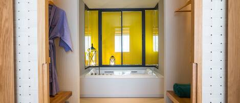 A modern bathroom with a large bathtub, wooden shelves, and a mirror with yellow curtains.