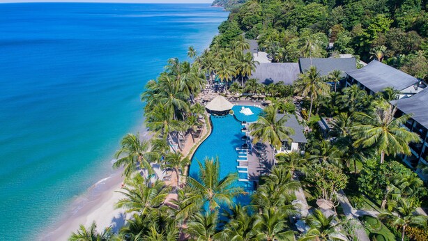 Vue aérienne d’un complexe hôtelier doté d’une piscine, d’une plage et d’une végétation luxuriante.