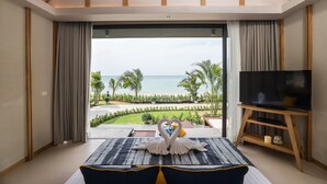 Une chambre avec une grande fenêtre, un lit, un téléviseur posé sur un meuble en bois, et une vue sur la plage.