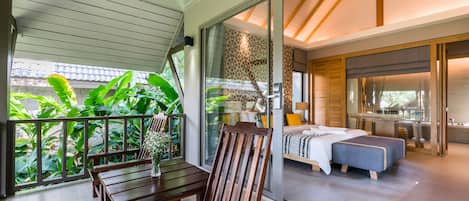 A modern bedroom with a large bed, a small seating area with a bench and table, and a balcony with plants.