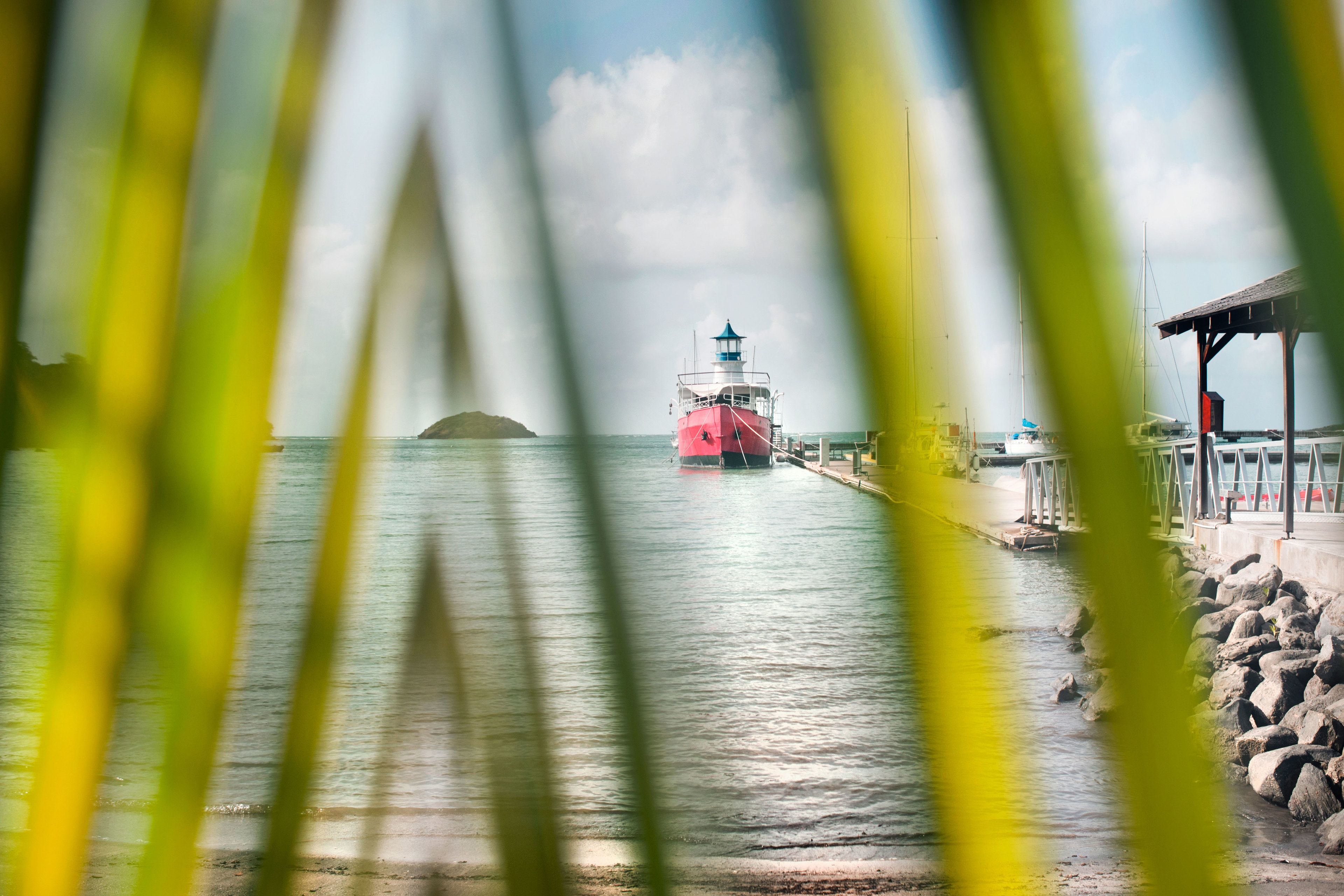 A lighthouse at a harbor with a rocky shoreline and a pier.