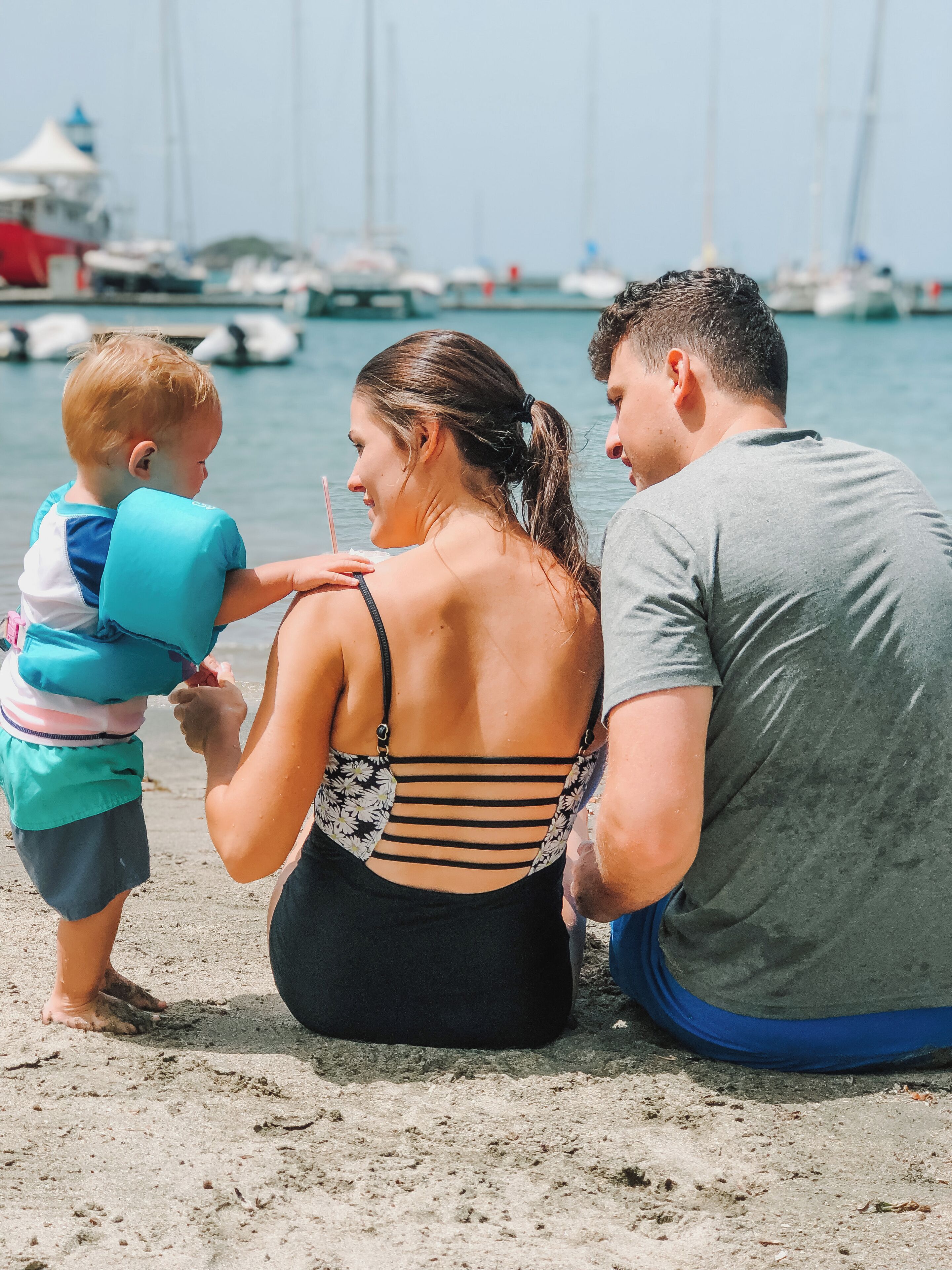 A family of three at a beach with boats in the background.