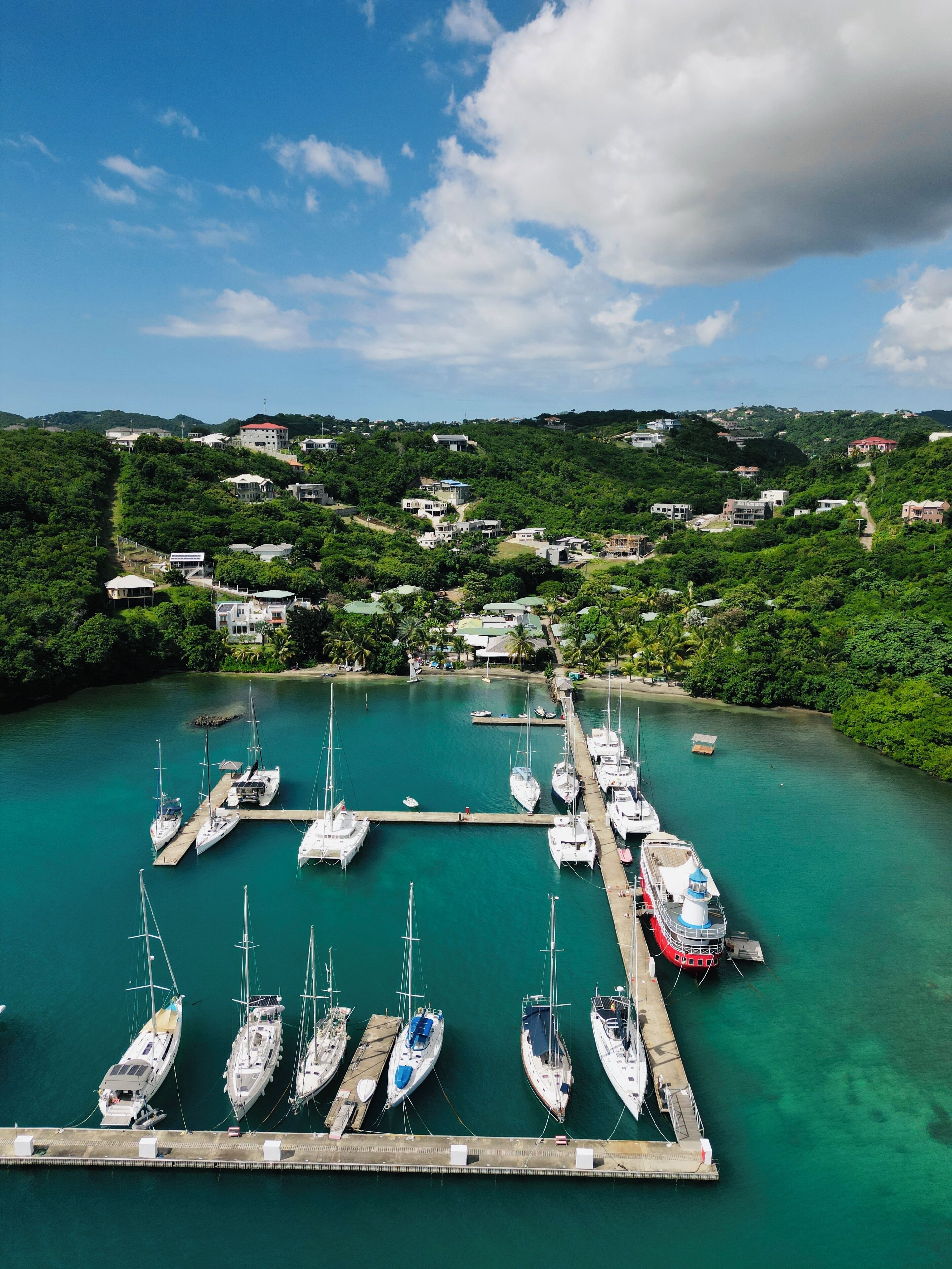 A marina with multiple boats docked, surrounded by lush greenery and hills in the background.