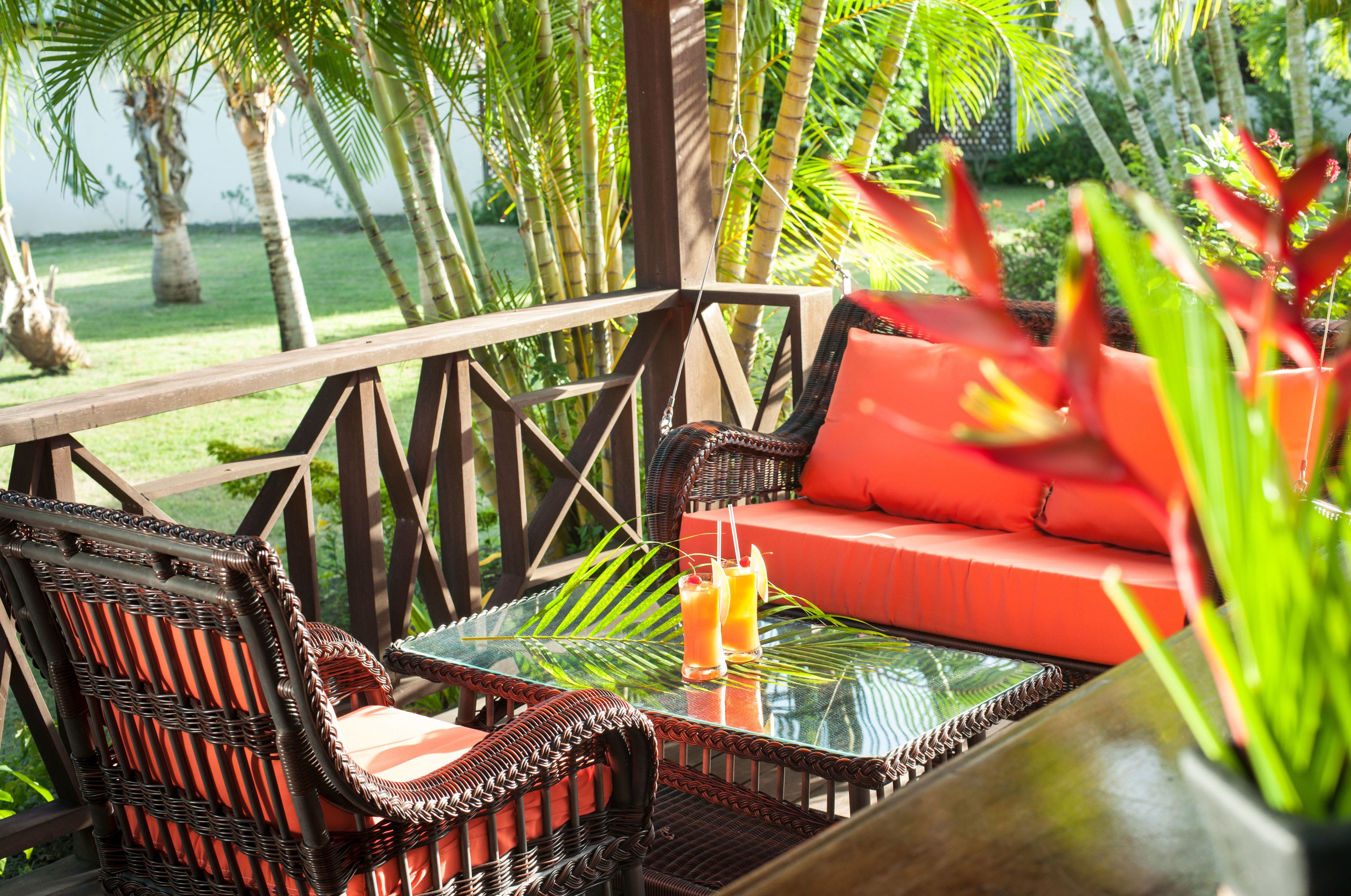 A tropical outdoor seating area with wicker furniture and a glass table, surrounded by lush greenery.