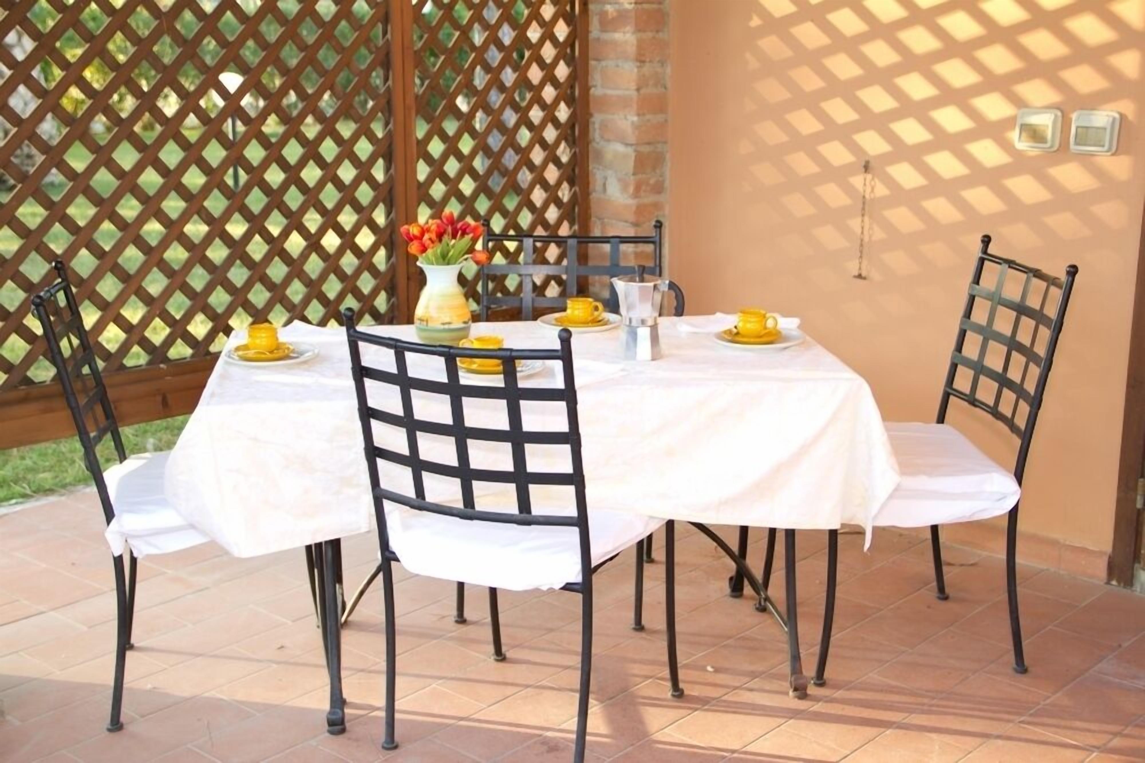 A round table with a white tablecloth, surrounded by four chairs with black metal frames.