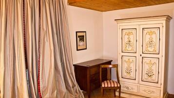 A room with a wooden ceiling, a bed with striped curtains, a wooden cabinet with decorative panels, and a chair with a striped cushion.