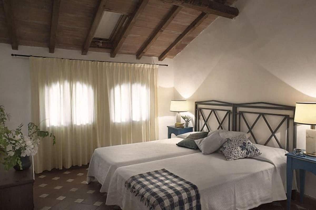 Une chambre avec deux lits, un plafond en bois, une fenêtre avec des rideaux et des lampes de chevet.