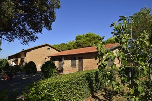 Un bâtiment en briques de deux étages, surmonté d’un toit recouvert de tuiles rouges, et entouré de verdure et d’arbres.