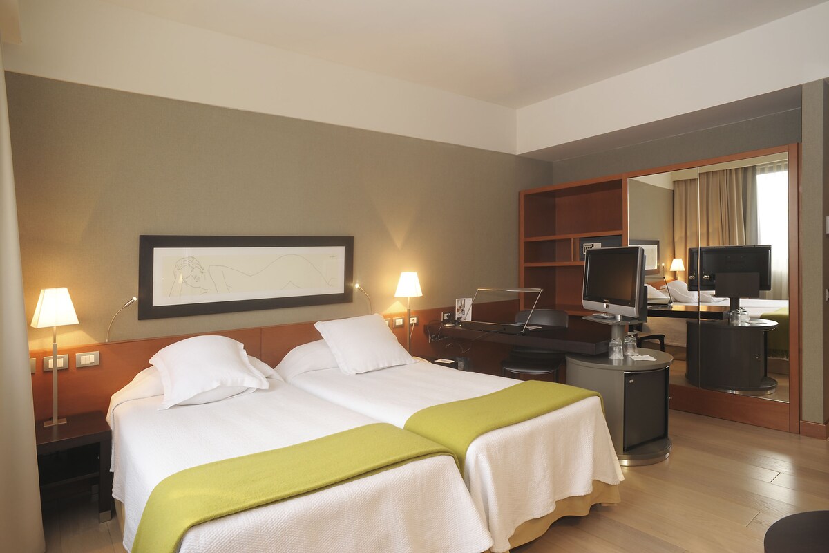 Une chambre d’hôtel avec deux lits, un bureau avec un ordinateur, une télévision et un miroir.
