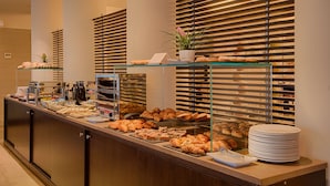 A buffet counter with various pastries and bread, a coffee station, and a stack of plates.