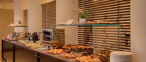 A buffet counter with various pastries and bread, a coffee station, and a stack of plates.