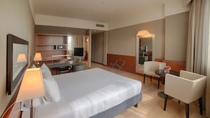 A hotel room with a large bed, a desk with a computer, a chair, and a small table with a vase.