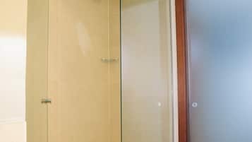A glass-enclosed shower with a handheld showerhead and a towel on the floor.
