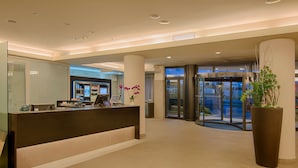 A modern hotel lobby with a reception desk, a large potted plant, and a revolving door.