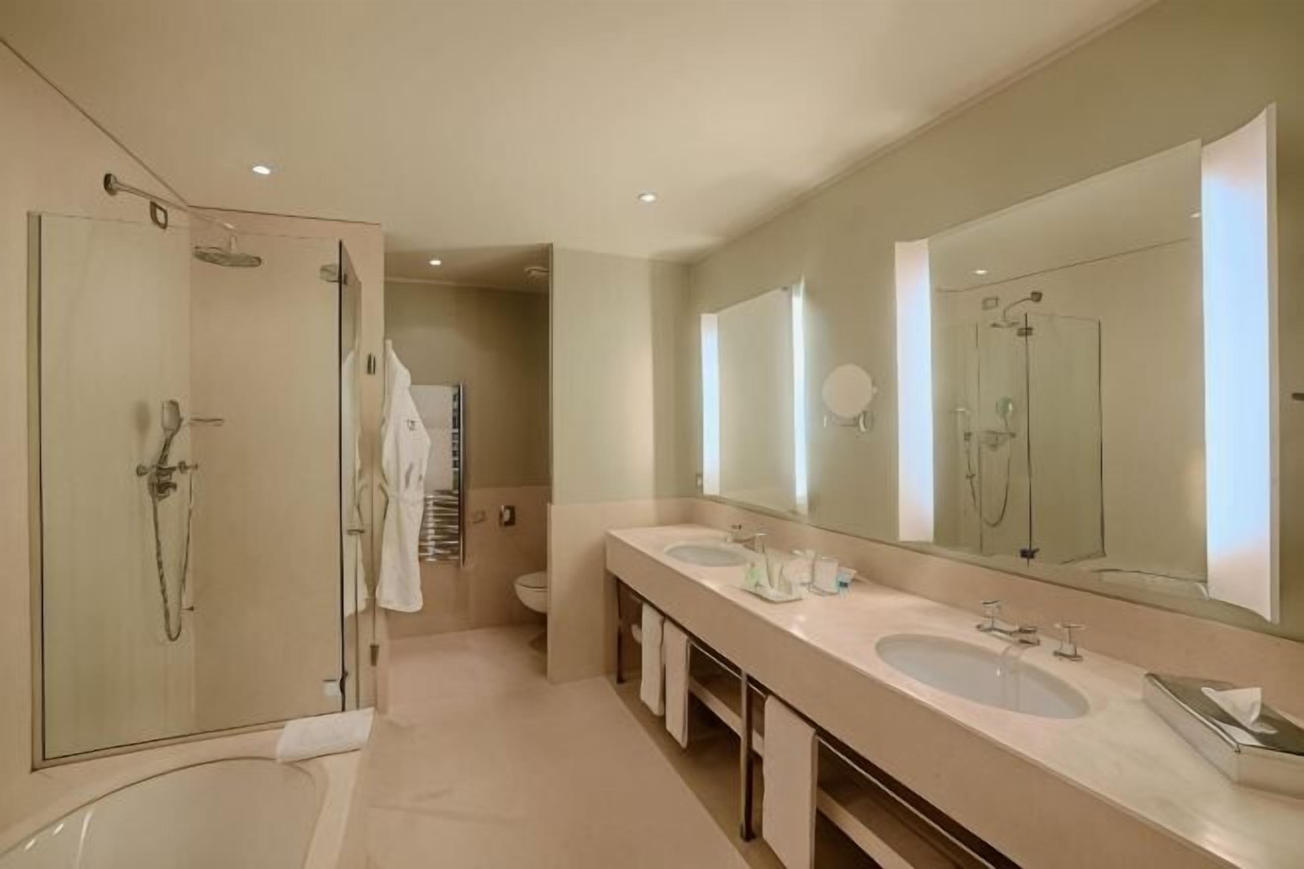 A modern bathroom with a glass-enclosed shower, two sinks, a large mirror, and a toilet.