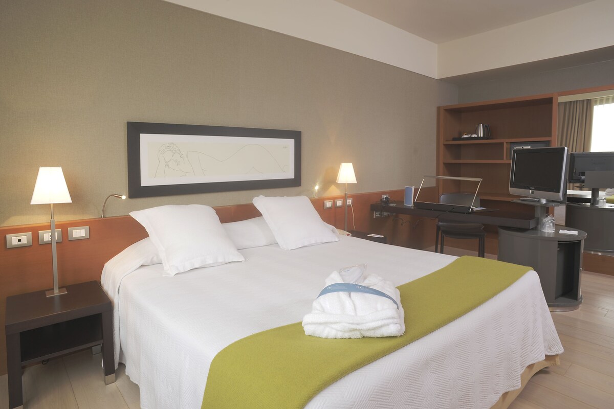 Une chambre d’hôtel comprenant un lit, deux lampes de chevet, un bureau avec un ordinateur et un téléviseur.