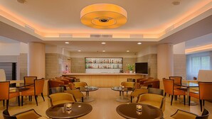 A modern hotel lobby with round tables and chairs, a bar area with a variety of bottles, and a large ceiling light.
