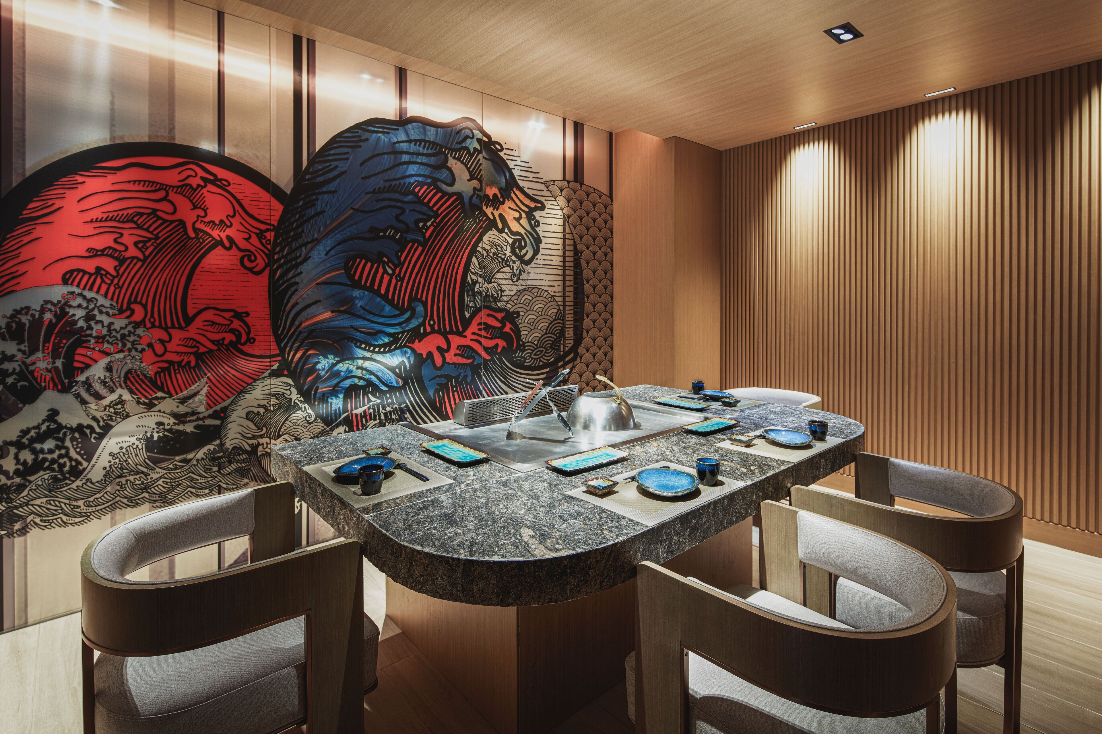 A modern dining area with a curved granite table, four chairs, and a decorative wall with traditional artwork.