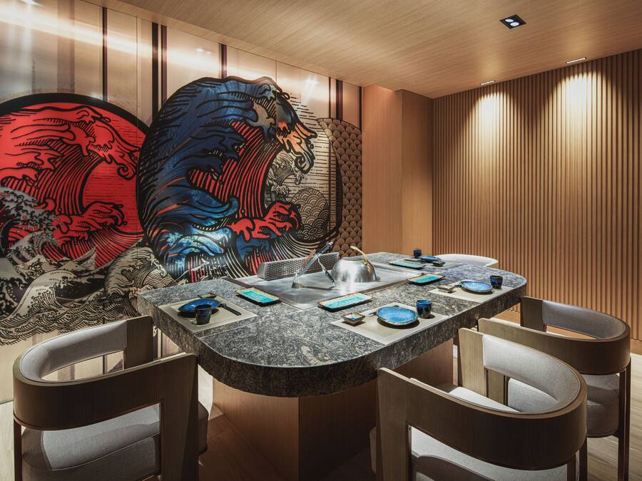 A modern dining area with a curved granite table, four chairs, and a decorative wall with traditional artwork.