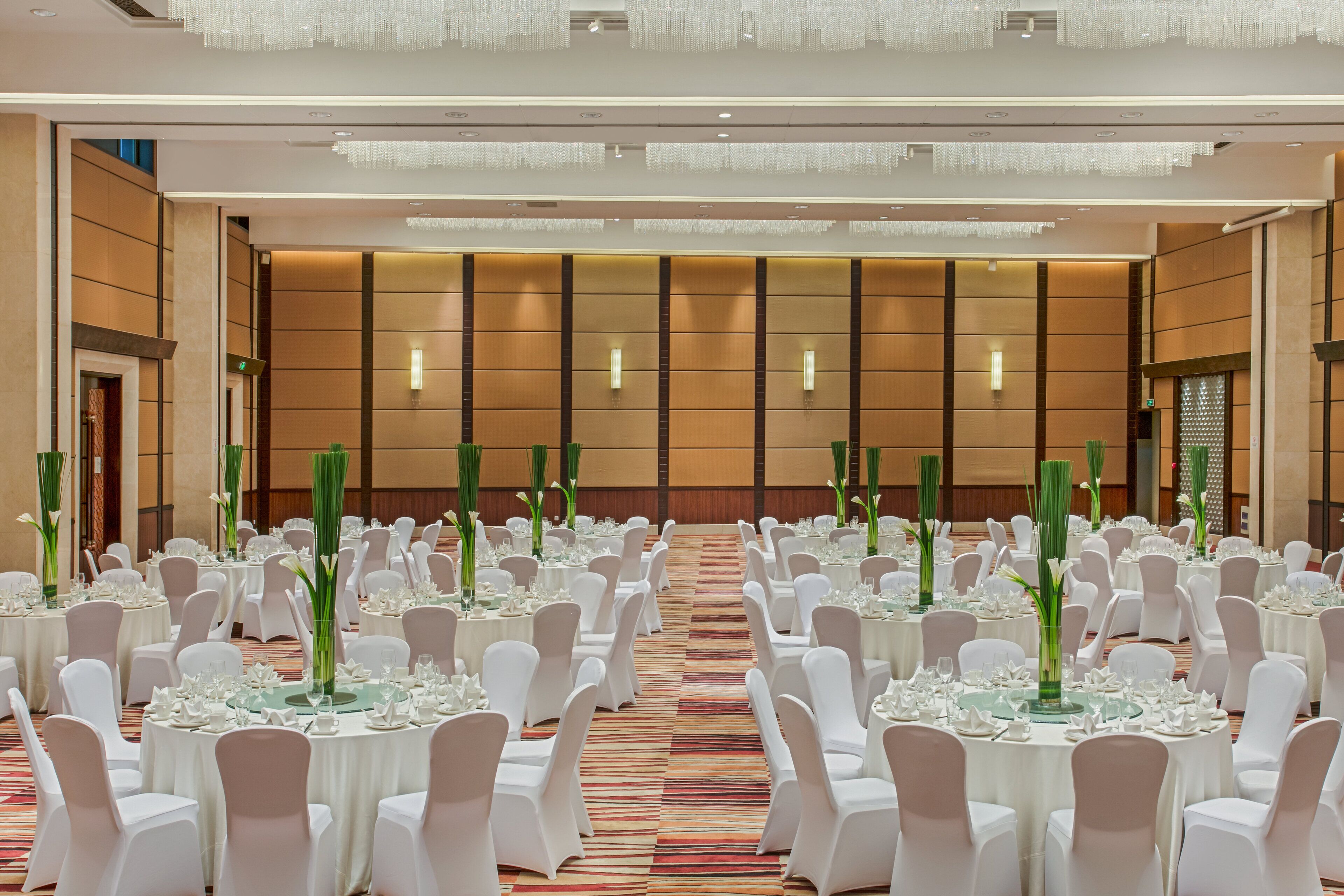 A banquet hall with round tables set for events, white chairs, and tall green floral centerpieces.