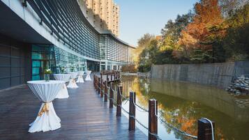A waterfront deck with tables and chairs, a chain barrier, and a building with a curved facade.