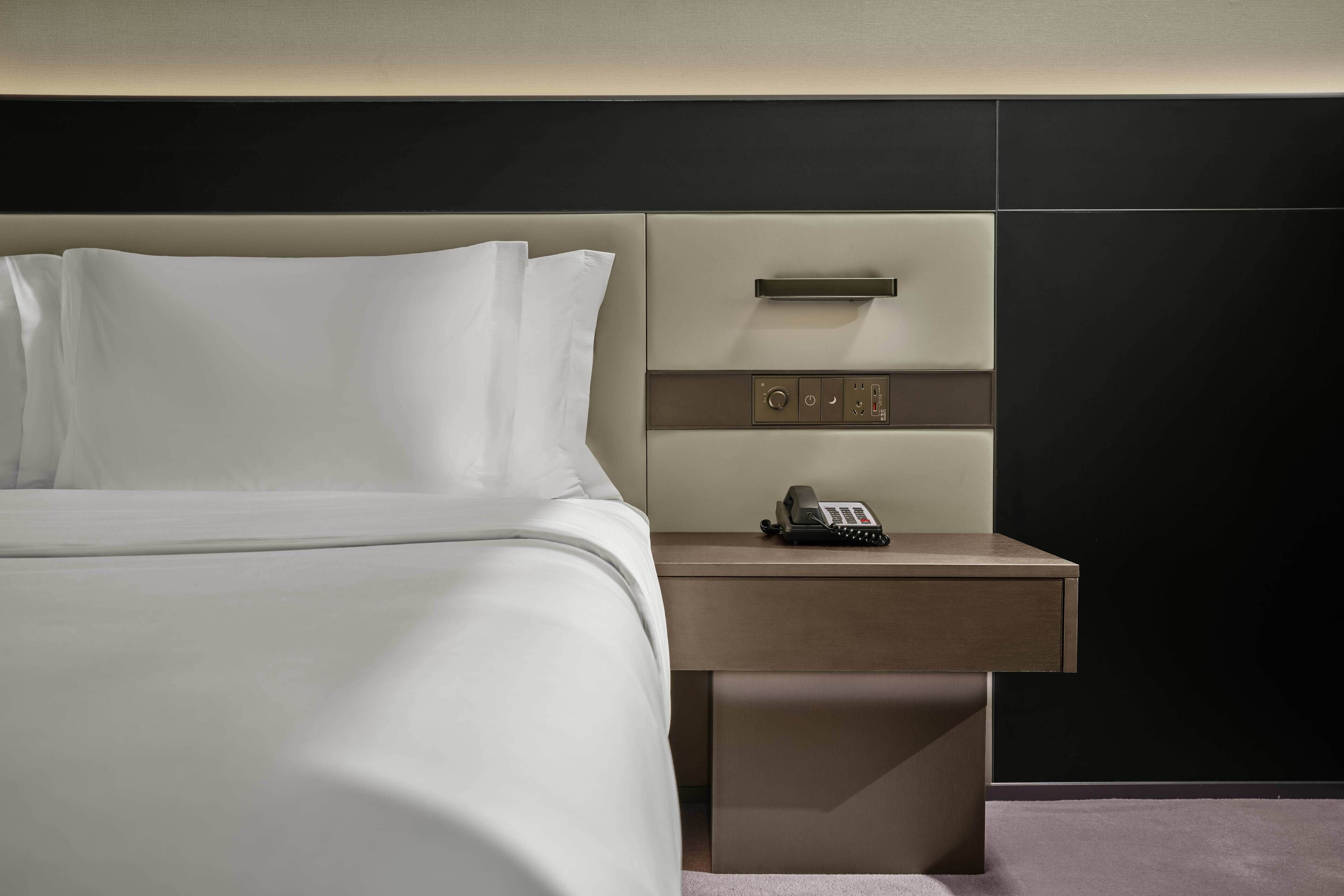 A hotel room with a neatly made bed, a bedside table with a phone, and a modern design.