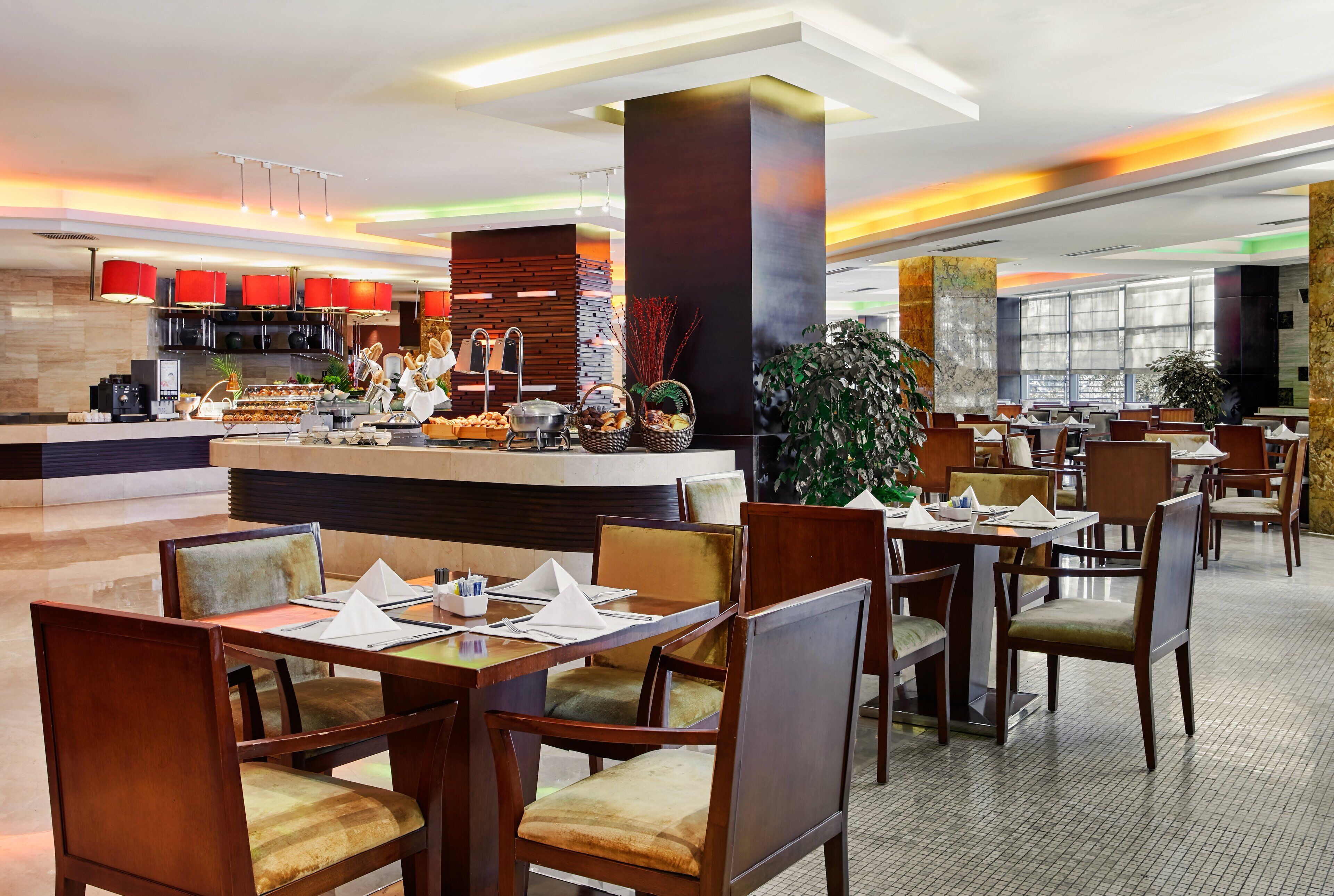 A modern restaurant with wooden furniture, a central counter, and large windows.