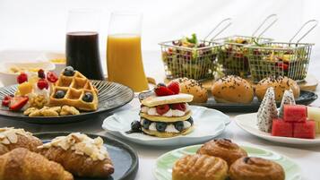 Buffet de café da manhã com waffles, doces, frutas e sucos.