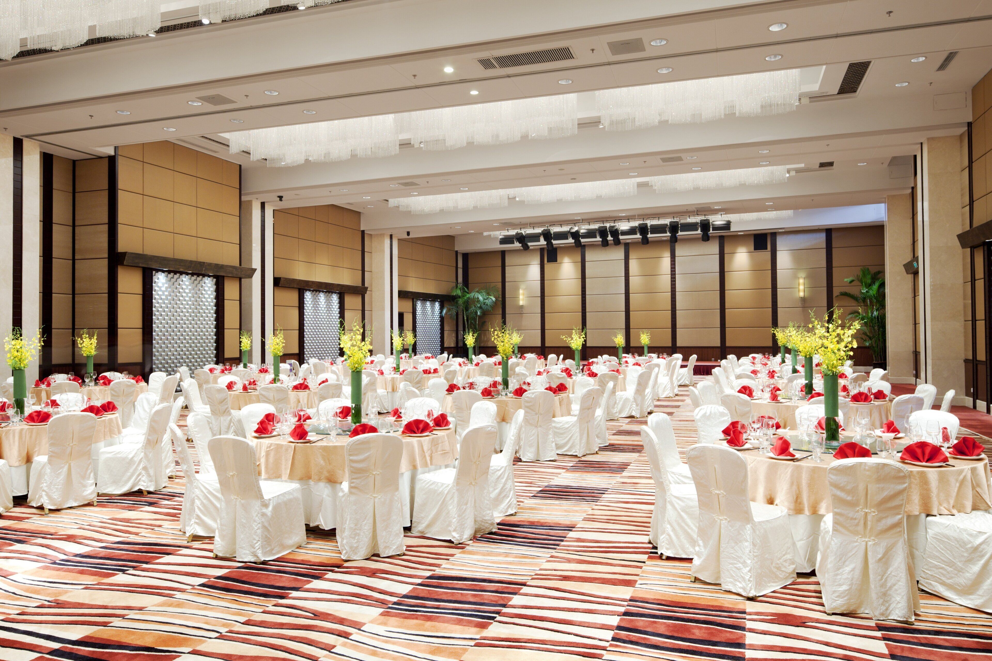 A banquet hall with round tables, white chairs, and red decorations.