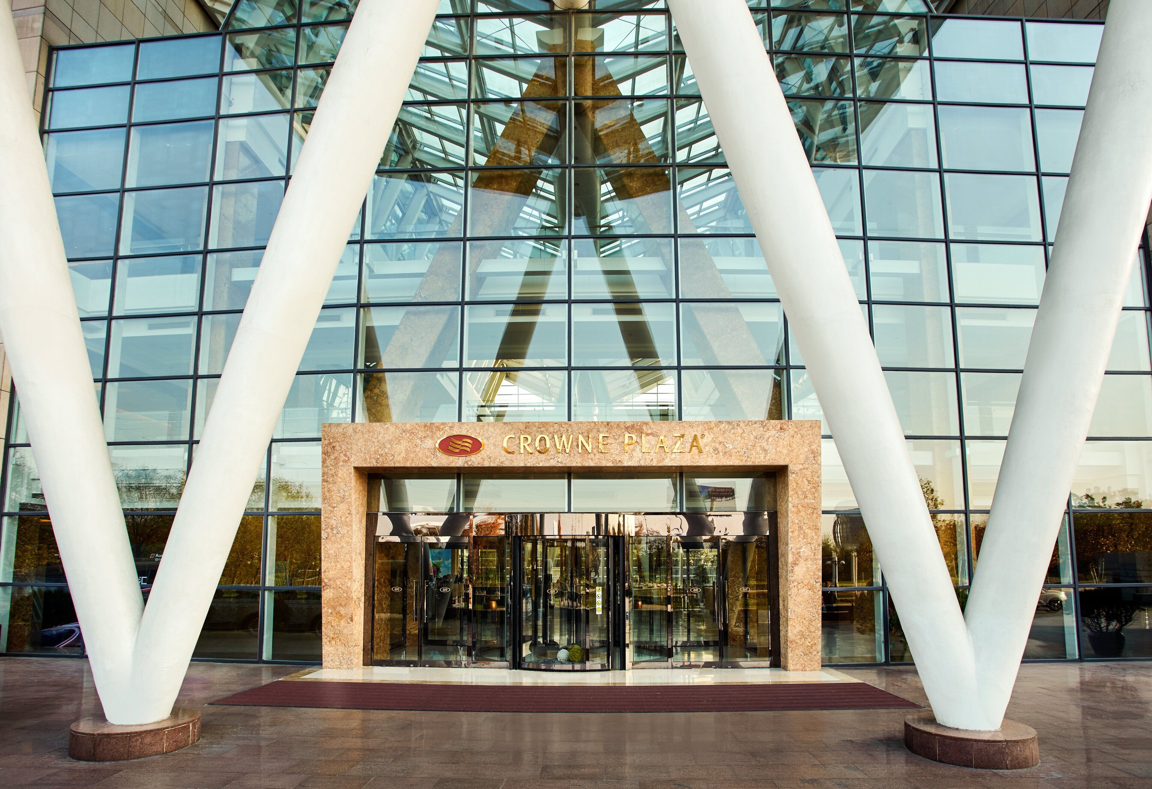 The entrance of Crowne Plaza with a glass facade and large white pillars.