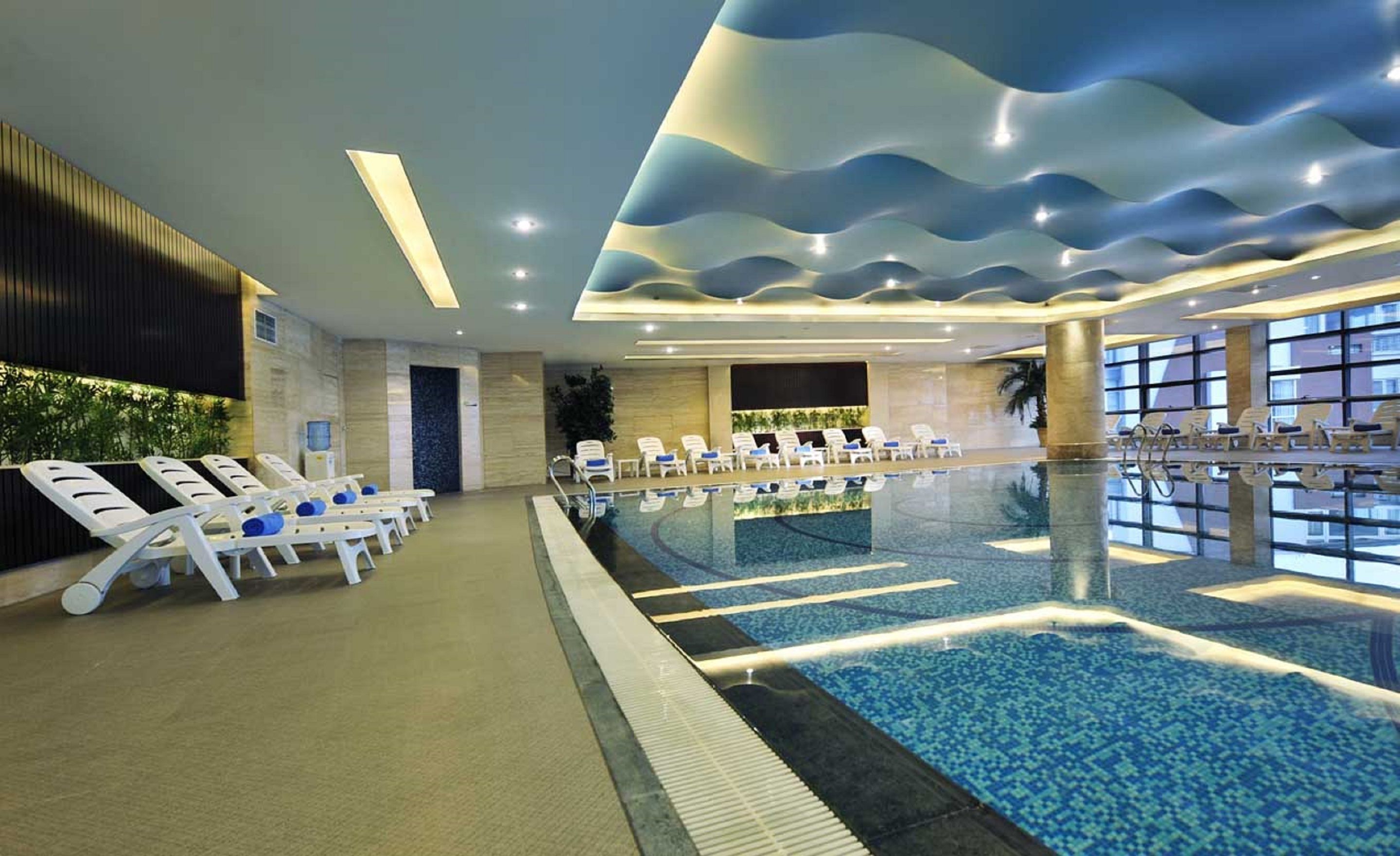 Ein Hallenbad mit Liegestühlen und einer wellenförmigen Deckenkonstruktion.