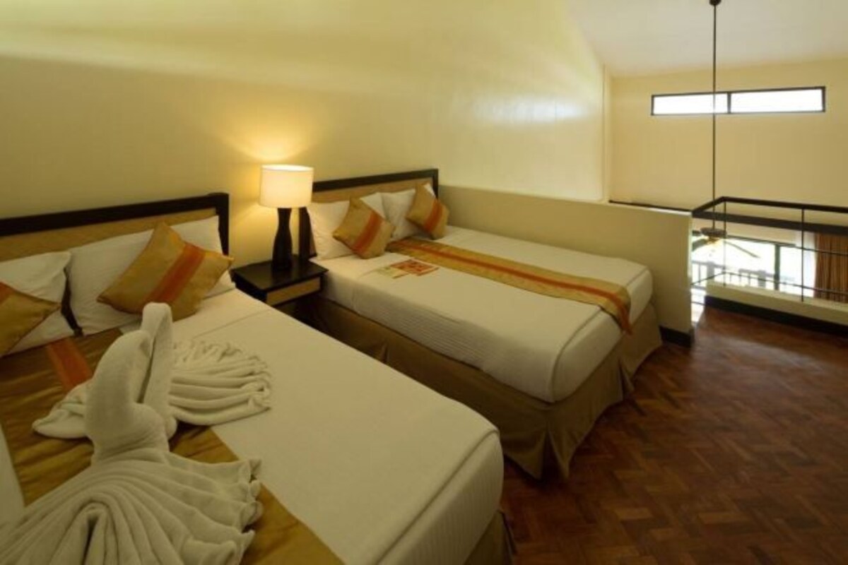 Habitación de hotel con dos camas, una mesita de noche con lámpara, una bata y un balcón con barandilla.