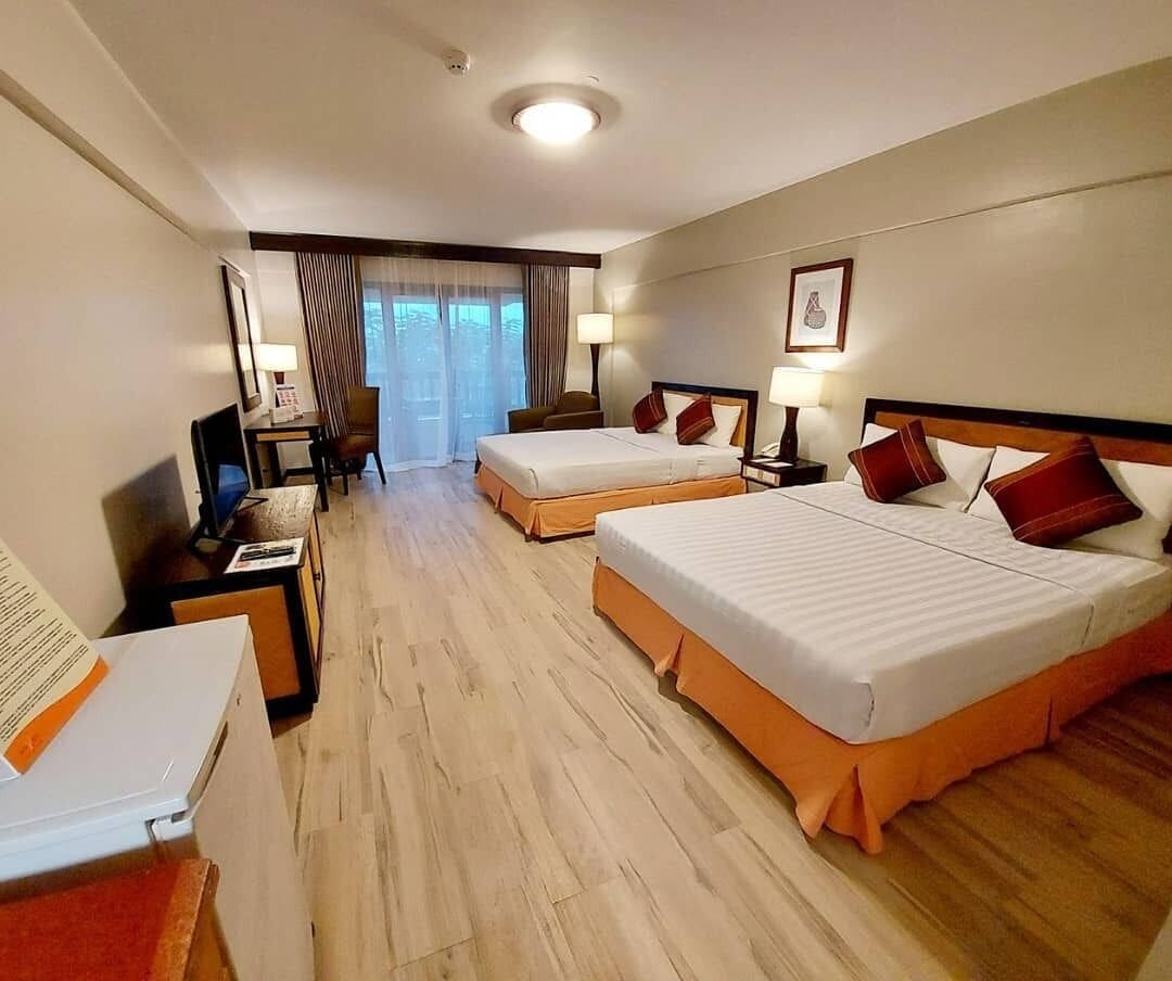 Habitación de hotel con dos camas, un escritorio con computadora, una silla y un ventanal con cortinas.