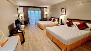 Habitación de hotel con dos camas, un escritorio con computadora, una silla y un ventanal con cortinas.