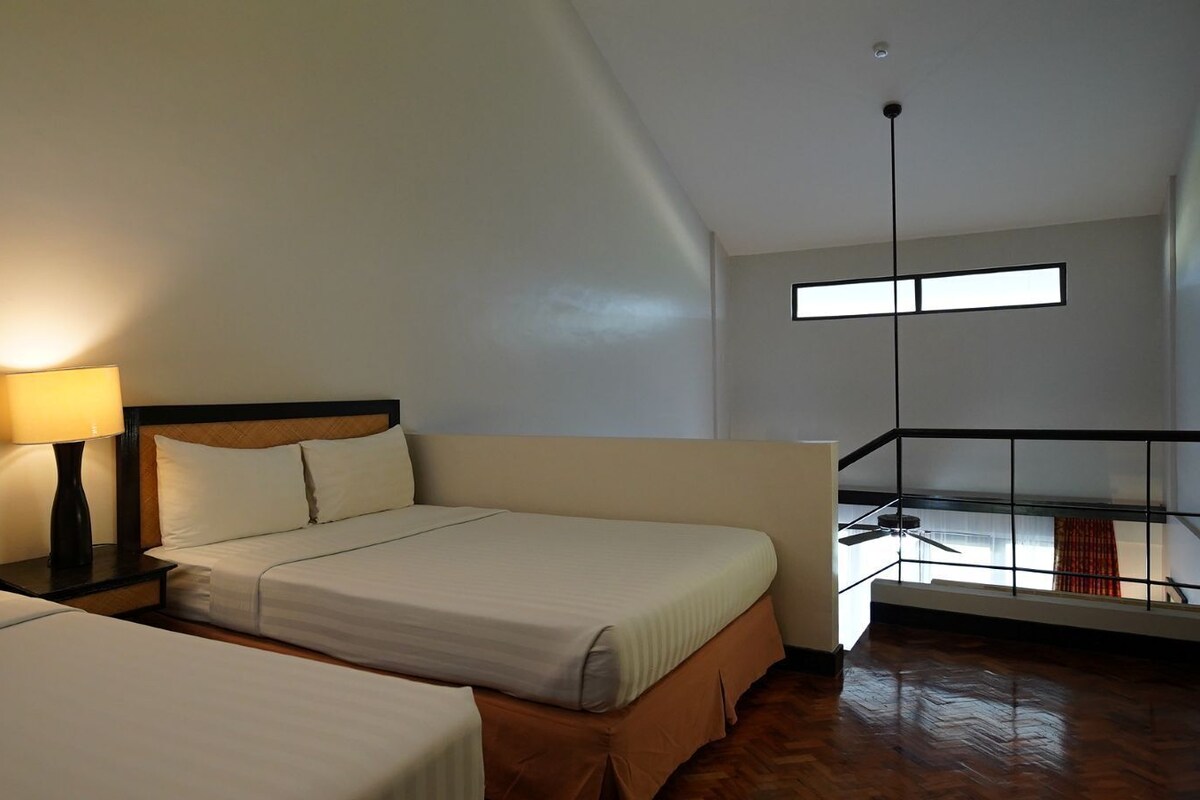 Une chambre d’hôtel avec deux lits, une table de chevet avec une lampe, un balcon avec vue et un ventilateur de plafond.