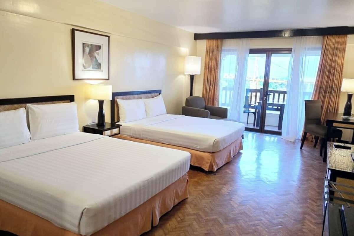 Habitación de hotel con dos camas, un escritorio, una silla, una lámpara y vistas al exterior.