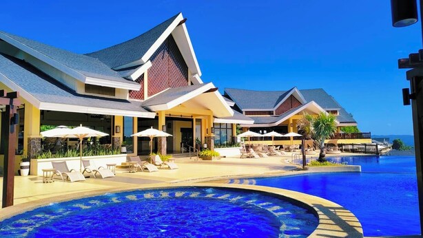 Un resort con una amplia piscina infinita, sillones de descanso y sombrillas.