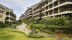 Un hotel con edificios de varios pisos, un jardín ajardinado con un sendero curvo y una variedad de plantas.
