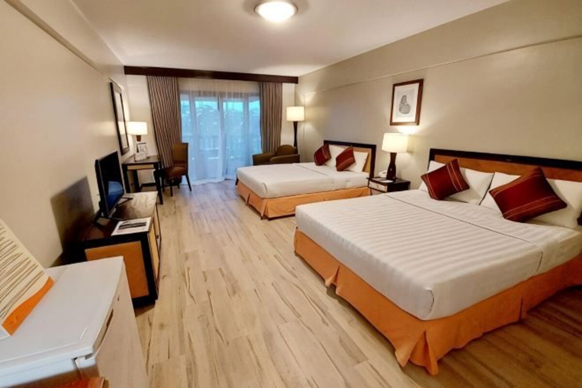 Habitación de hotel con dos camas, un escritorio, una silla, un televisor y una ventana con cortinas.