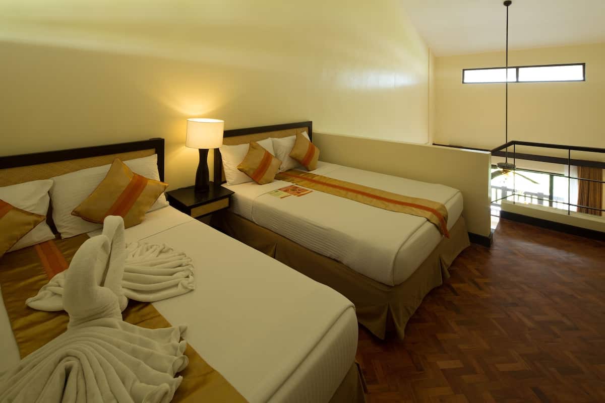 Una habitación de hotel con dos camas, una mesita de noche con lámpara, ventana con vistas y suelo de madera.