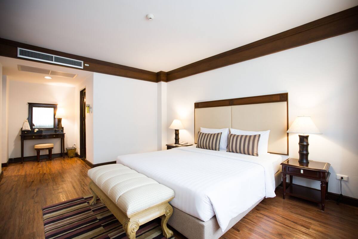 A hotel room with a large bed, a desk with a chair, a mirror, and two bedside lamps.