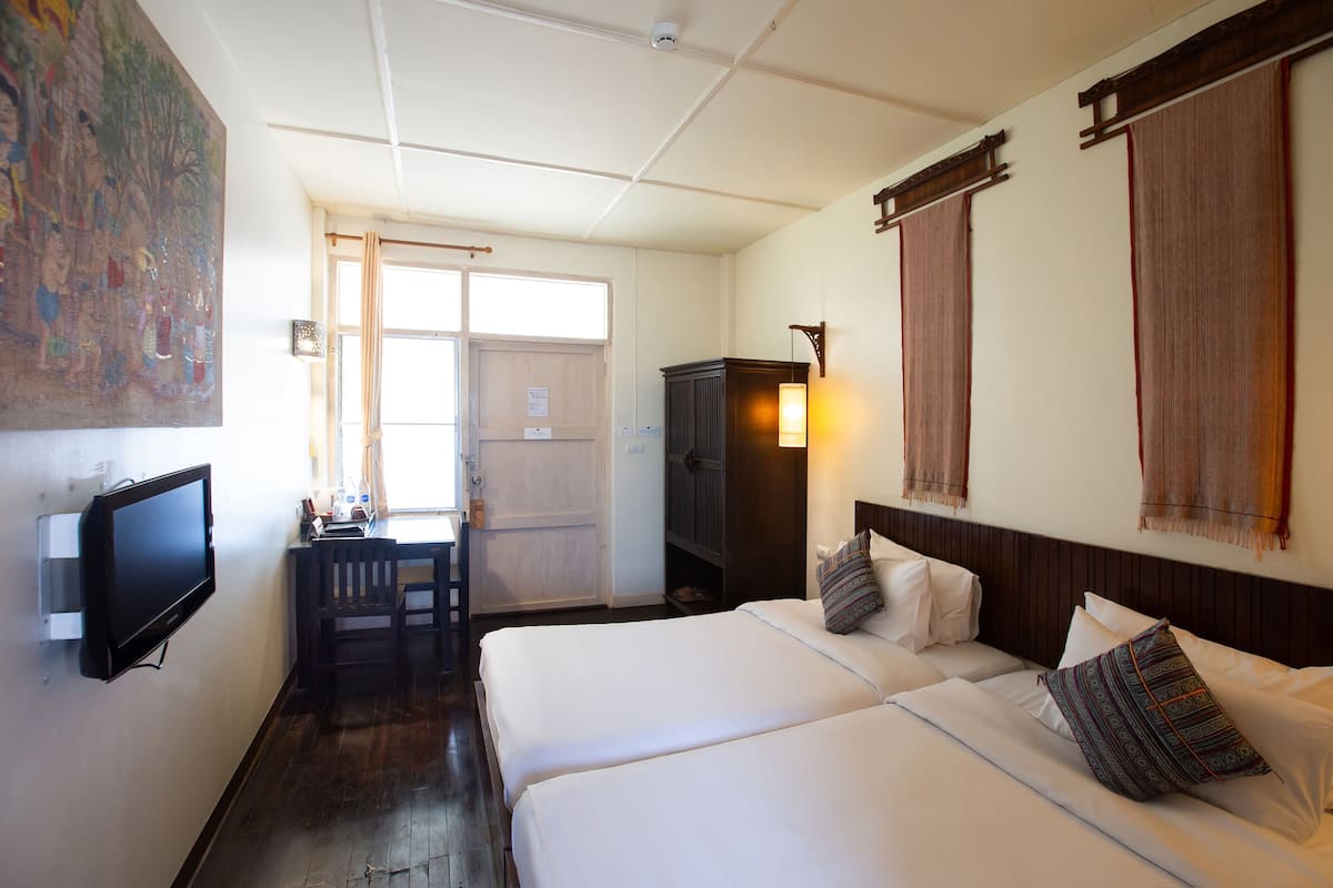 A hotel room with two beds, a TV, a desk, and a large painting on the wall.