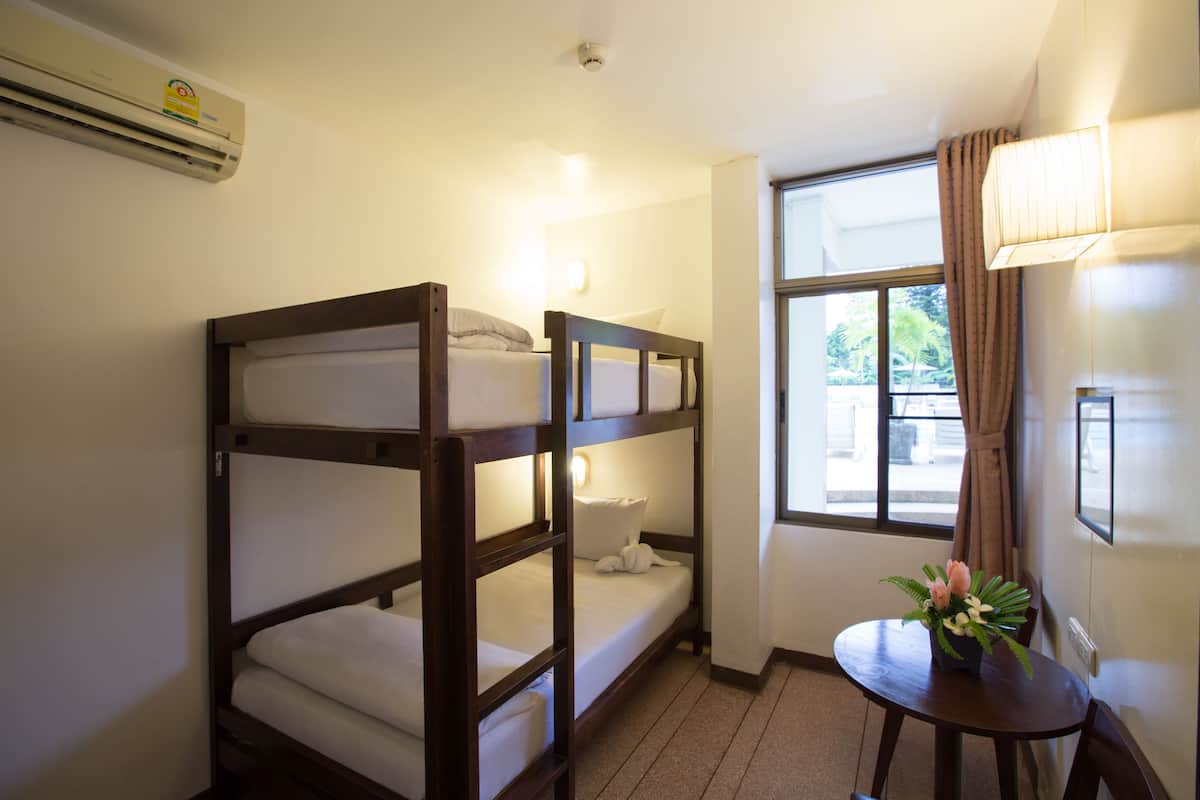 A bunk bed room with a window, a table with a flower vase, and a wall-mounted air conditioner.