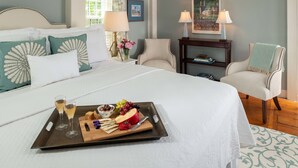 A hotel room with a large bed, a bedside table with a lamp, a chair, and a tray with snacks and drinks. - The Inn at Yarmouth Port (Yarmouth Port)