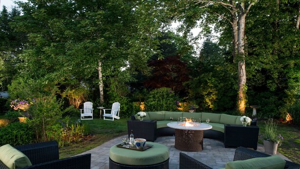 An outdoor patio area with wicker furniture, a round table with a fire pit, and a white chair. - The Inn at Yarmouth Port (Yarmouth Port)