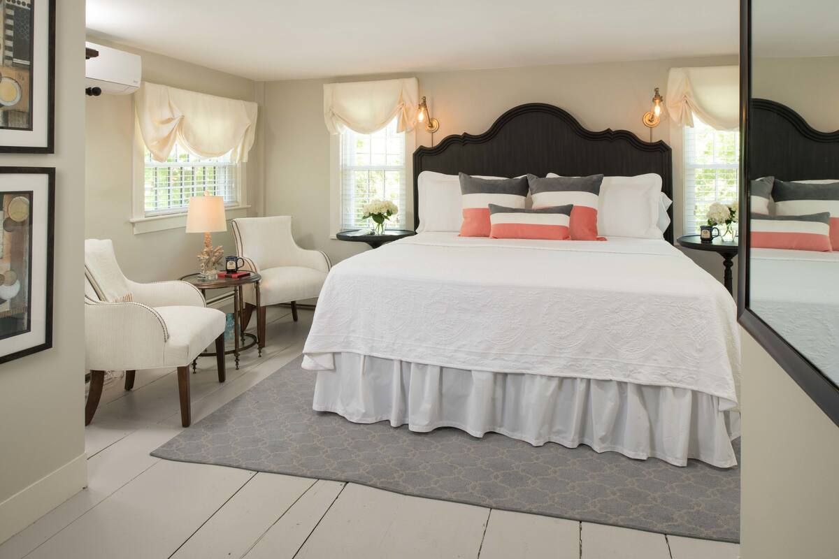 A spacious bedroom with a large bed, two bedside tables, a chair, and a window with curtains.