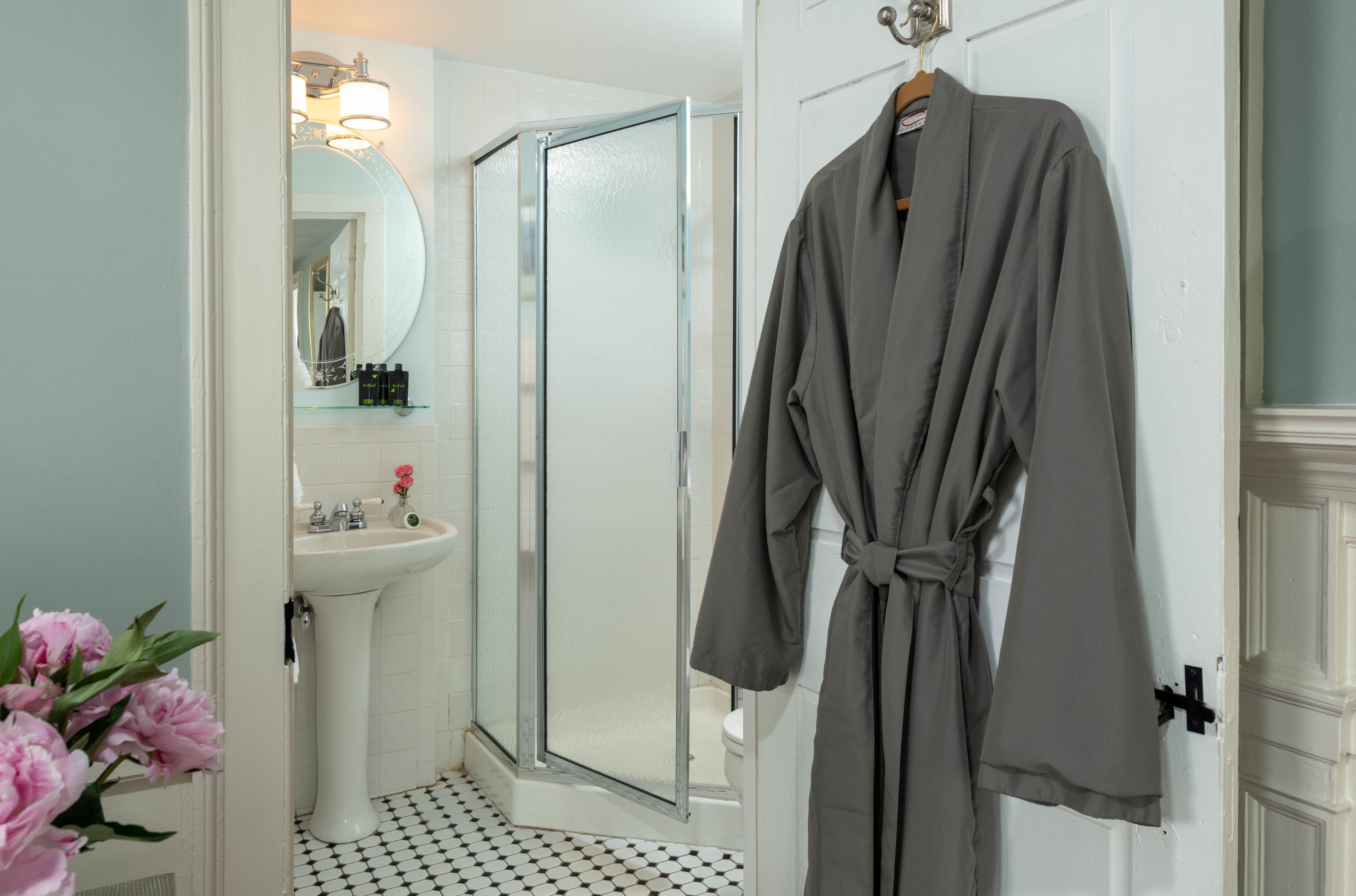 A bathroom with a white sink, a glass shower enclosure, and a robe hanging on a door.